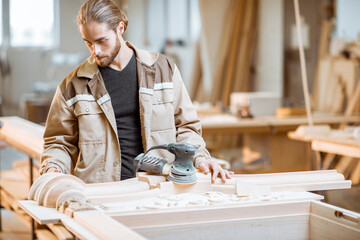 Handsome carpenter checks out carving quality of a joiner's product at the carpentry manufacturing