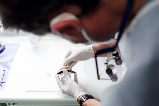 Mature prosthodontist making denture while standing at clinic