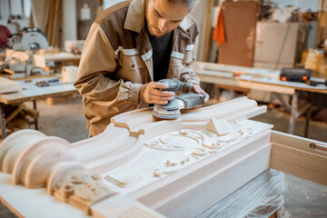 Carpenter grinding joinery product with carvings, finishing woodwork at the carpentry manufacturing