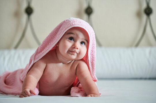 Baby girl in towel looking up while lying on bed at home