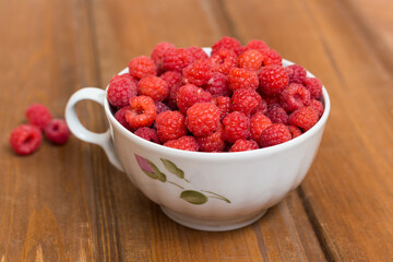 Juicy red raspberries in a white mug on a wooden table