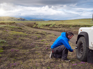 Male tourist kneeling while examining tire pressure through equipment at roadside
