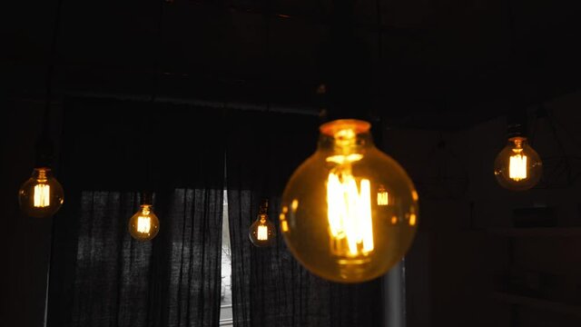 Big vintage incandescent light bulbs hanging in the dark kitchen. Decorative antique edison light bulbs with straight wire. Inefficient filament light bulbs waste electricity. Warm white dimmable, led