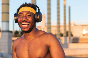 Shirtless man wearing headphones laughing while standing at park