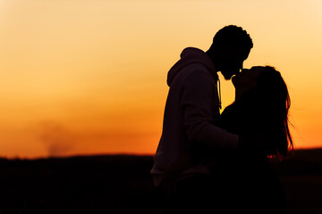 Fototapeta na wymiar Silhouettes of lovely couple, handsome man kiss beautiful woman at sunset, enjoy tender moments, caring husband and loving wife spend time together, weekends outdoors concept