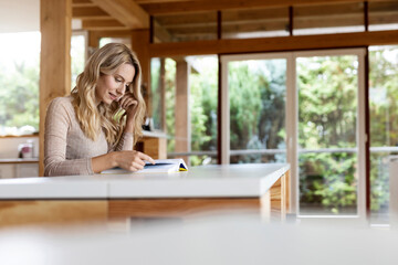 Beautiful woman reading book while sitting by table at home