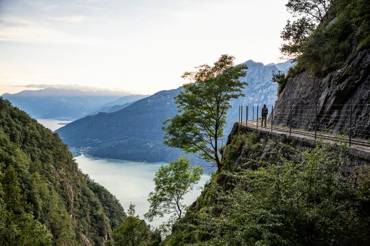 Italy, Province of Sondrio, Silhouette of hiker admiring Lake Mezzola from fenced edge ofÔøΩTracciolino trail
