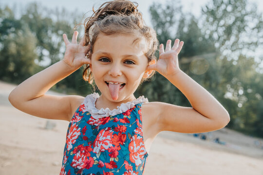 Cute little girl sticking out tongue while standing at beach