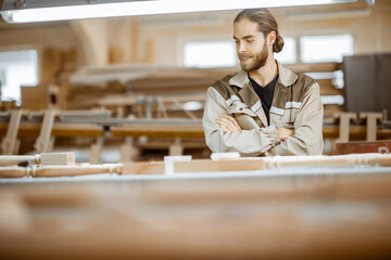 Portrait of a handsome manual worker at the workspace, finishing wooden products at the carpentry manufacturing