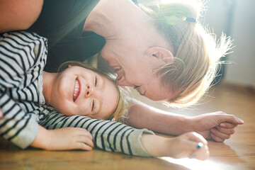 Happy mother playing with daughter while lying on floor at home