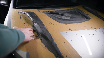 designer is making form of car hood for tuning service, covering surface by modeling clay, shaping by plastic blade