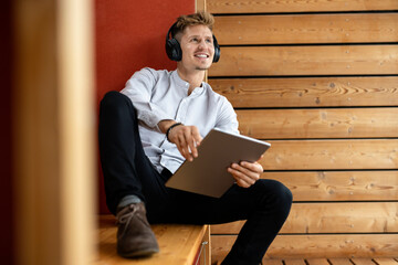 Man wearing headphones with digital tablet looking away while sitting at home