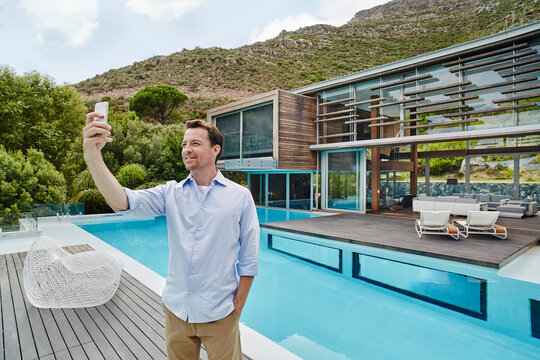 Mature man taking selfie on smart phone while standing against modern house