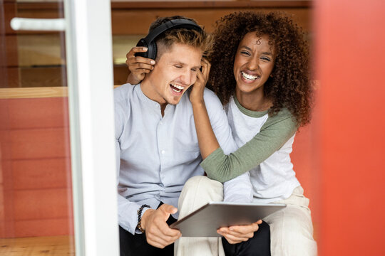 Playful woman sitting by man working on digital tablet at home