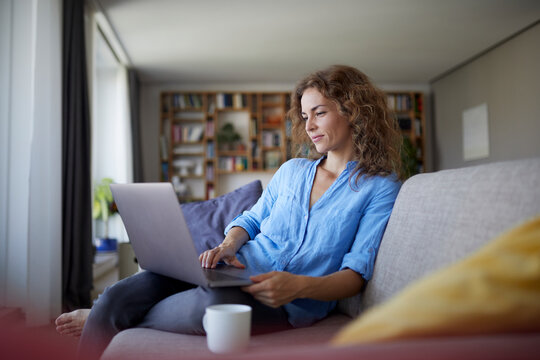 Mid adult woman using laptop while sitting on sofa at home