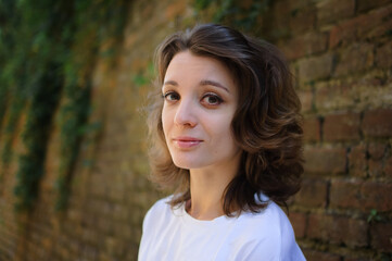 Female portrait of beautiful student, pretty girl with short hair in white t-shirt spending time outdoors near old stone wall during sunny spring or summer day