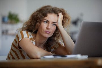 Tired woman with head in hand sitting by table at home