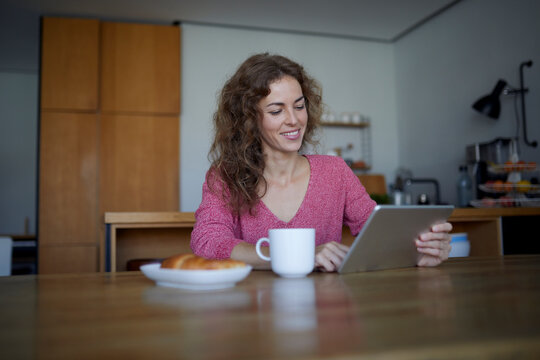 Woman with food and coffee using digital tablet while sitting at home