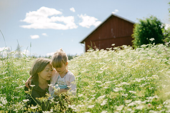 Woman with daughter amidst wildflowers growing on field during sunny day