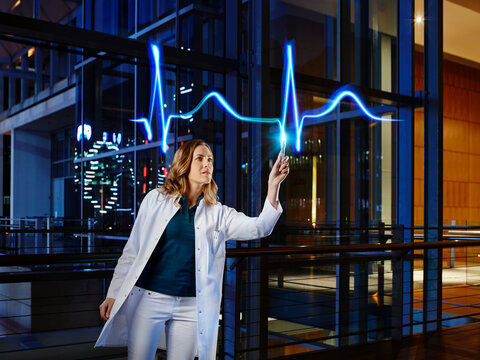 Female doctor examining pulse trace with light painting at hospital