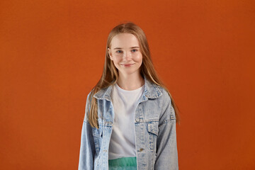 Portrait of a beautiful cute girl, smiling and looking at the camera. Bright orange background.