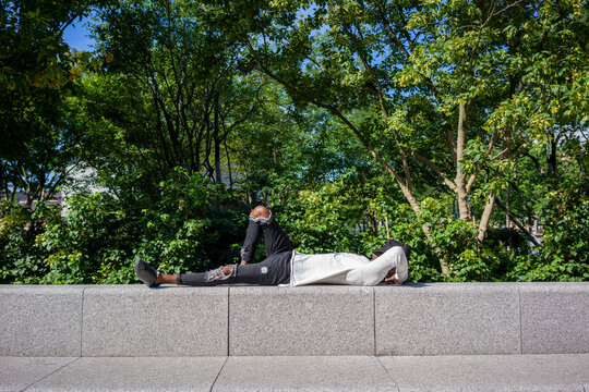 Man with cap on face lying on retaining wall at park