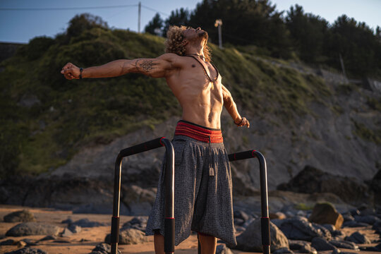 Shirtless muscular man standing with arms outstretched at beach
