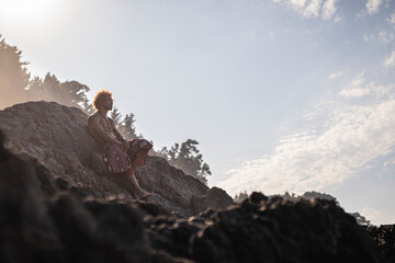 Young man leaning on rock formation against sky