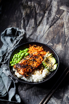 Bowl of teriyaki salmon with rice, carrot salad, edamame beans, avocado and sesame seeds