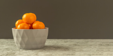 Fresh organic citrus mandarin oranges fruit in a gray bowl on a gray stone background. Selective focus, side view and copy space. Banner.