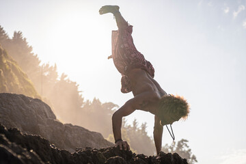 Young man practicing handstand on rock at beach against sky