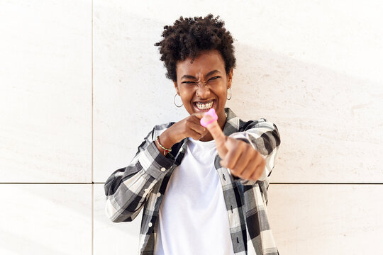 Carefree young woman throwing pink mask against white wall