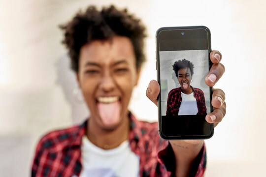 Cheerful young woman with tongue out showing her photograph on smart phone