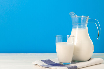 Glass and pitcher of milk against blue background