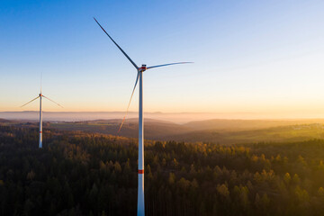 Wind turbines standing in autumn forest at dusk