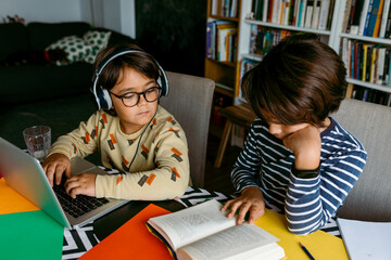 Boy peeking while male friend reading textbook at table