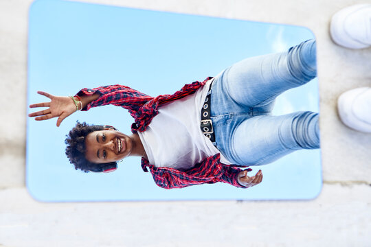 Playful young Afro woman waving at mirror reflection
