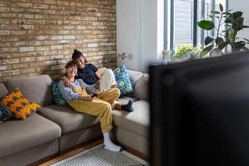 Smiling lesbian couple watching television while sitting on sofa at home