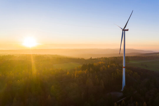 Setting sun illuminating wind turbine standing in autumn forest