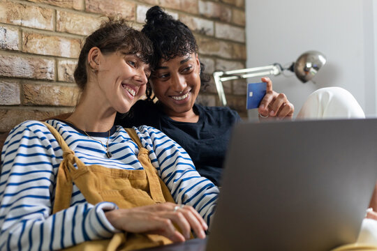 Lesbian couple looking at credit card while doing online shopping on laptop at home