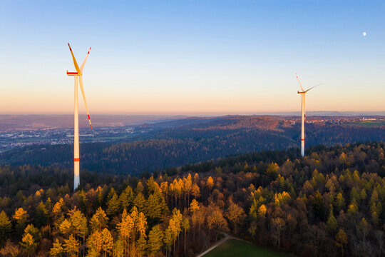 Wind turbines standing in autumn forest at dusk