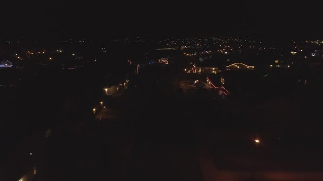 Santa and the reindeer fly over a suburban neighborhood just over the rooftops of houses decorated for the holidays.