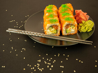 Rolls of fish and cucumber in orange caviar, on a gray plate