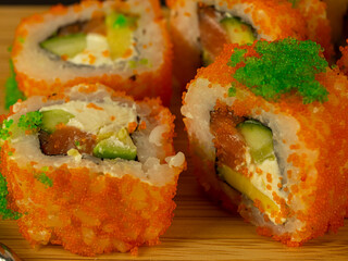 Rolls of fish and cucumber in orange caviar, on a wooden board