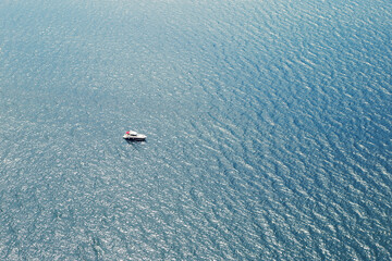 A yacht or a boat floats alone on the big water in sun glare. Open sea without wind.