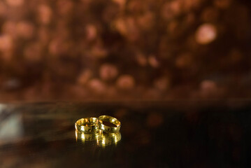 Golden wedding rings on sparkle bokeh background. Selective focus with copy space for text. Wedding card and invitation background. Pink color. 