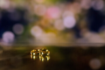 Golden wedding rings on sparkle bokeh background. Selective focus with copy space for text. Wedding card and invitation background. Pink color. 