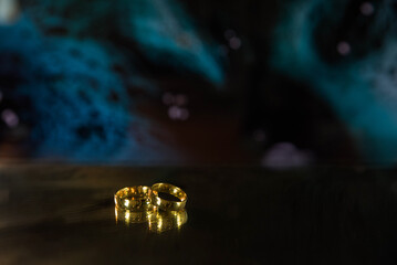 Golden wedding rings on sparkle bokeh background. Selective focus with copy space for text. Wedding card and invitation background. Blue color. 