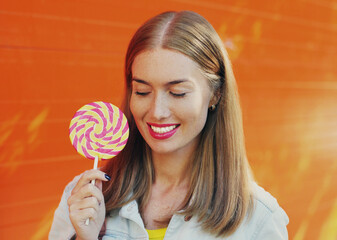 Summer colorful portrait of happy smiling young woman with lollipop over an orange background