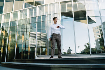 Caucasian businessman 30 years old checking time near office building using modern technology during work break in financial district, smart casual male entrepreneur looking at wearable equipment